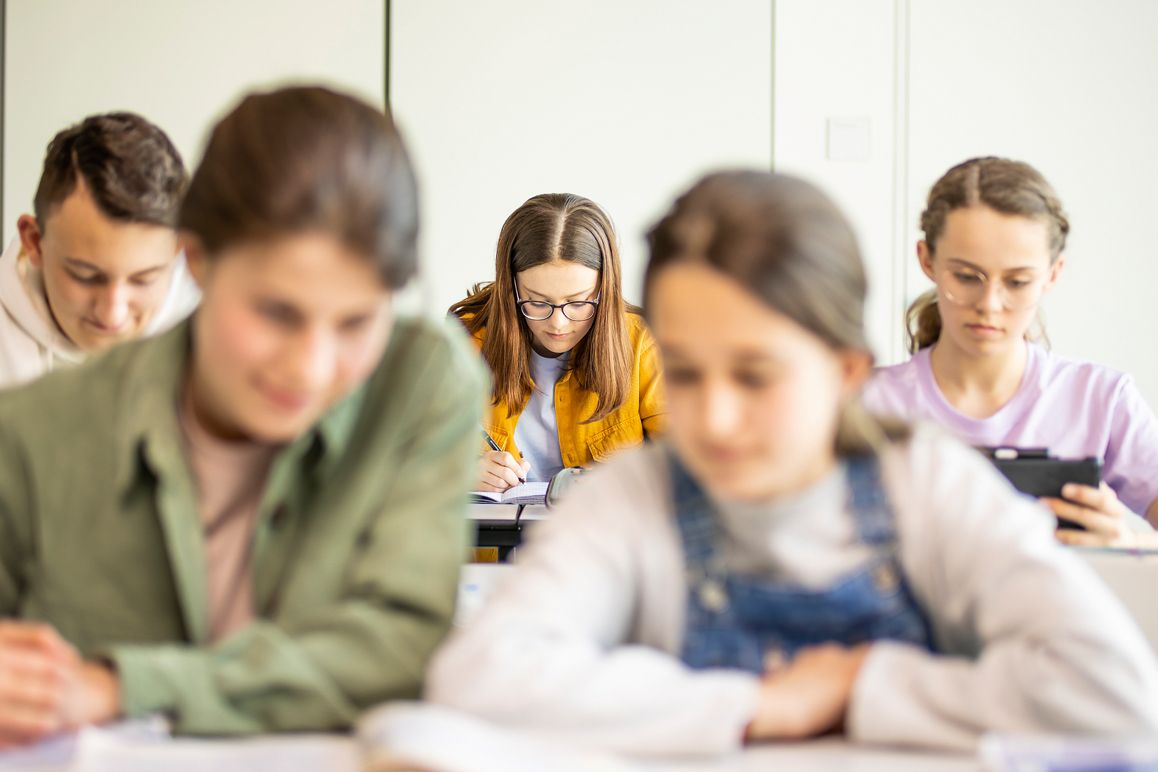 A group of students attentively seated at desks in a classroom, engaged in learning and collaboration.