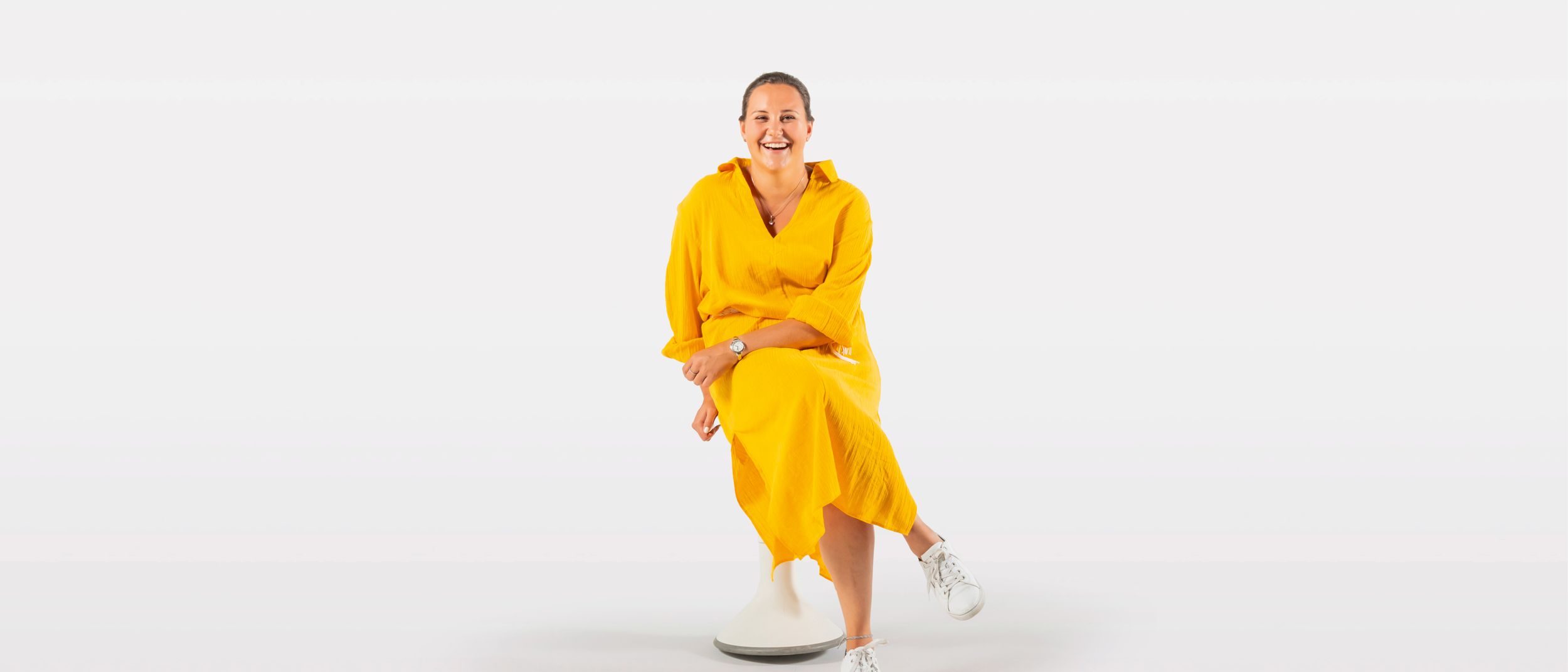 Young woman in a yellow dress sits on the ergonomic stool Hokki by VS