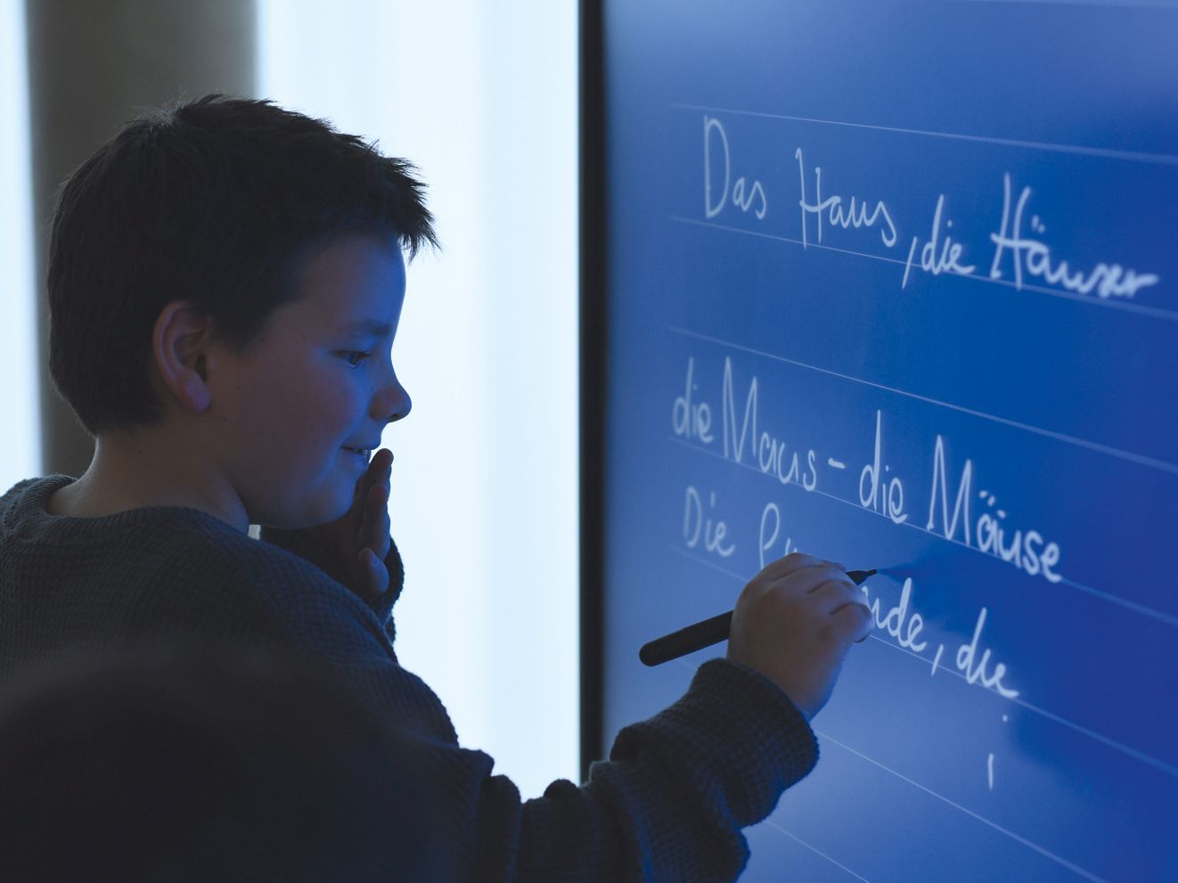 A boy writes on an interactive whiteboard.
