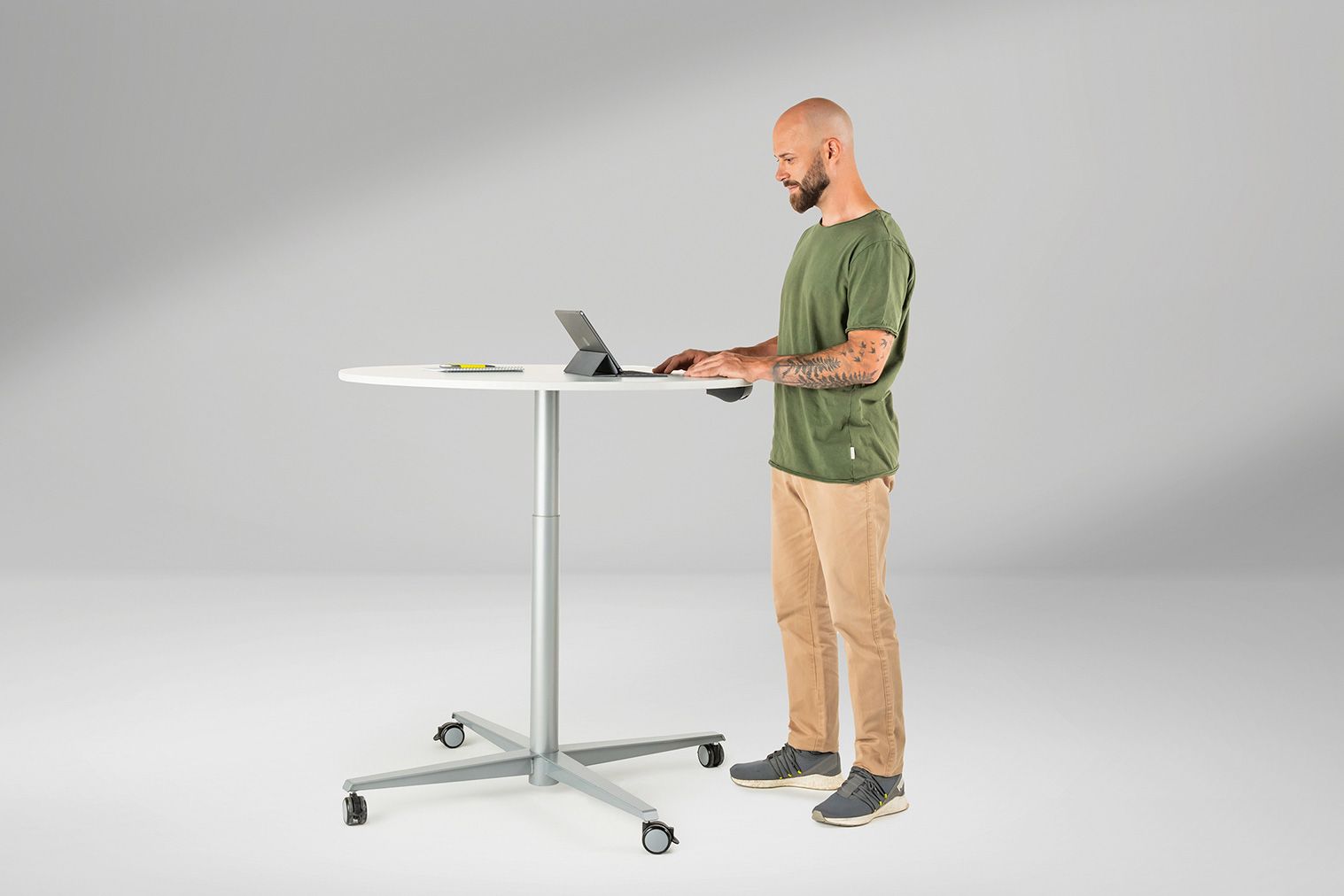 Ein Mann steht am höhenverstellbaren Mehrzwecktisch Rondo von VS und arbeitet an seinem Laptop.