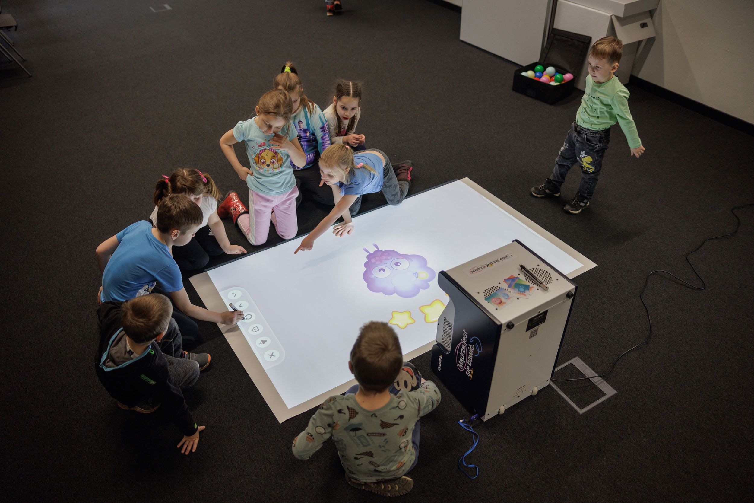 Kinder im Grundschulalter hocken am Boden um eine Projektion der Knowla-Box.