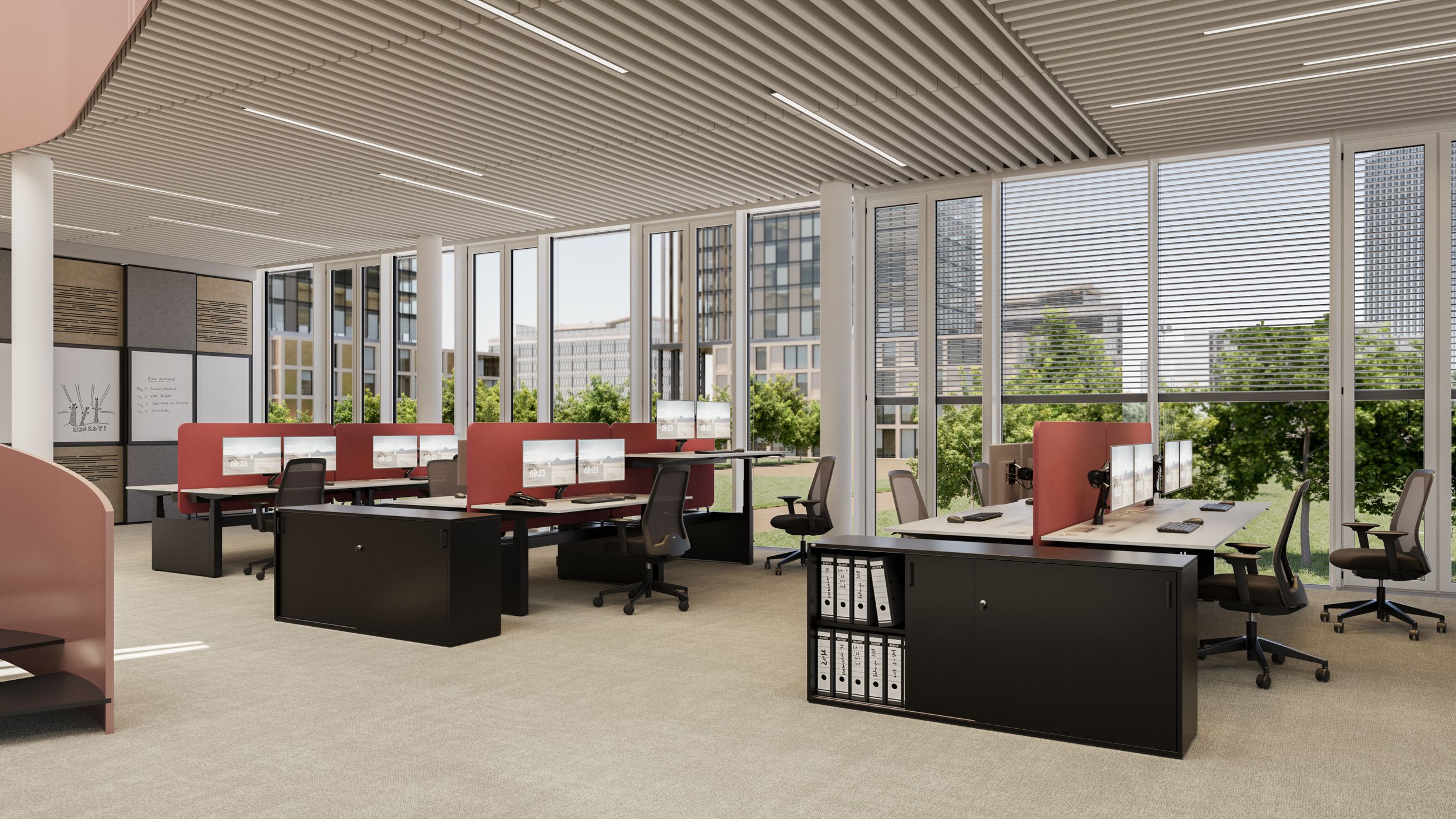 A bright, open-concept office with height-adjustable desks, red desk dividers, swivel chairs, and sideboards set against a large window wall with a view of greenery.