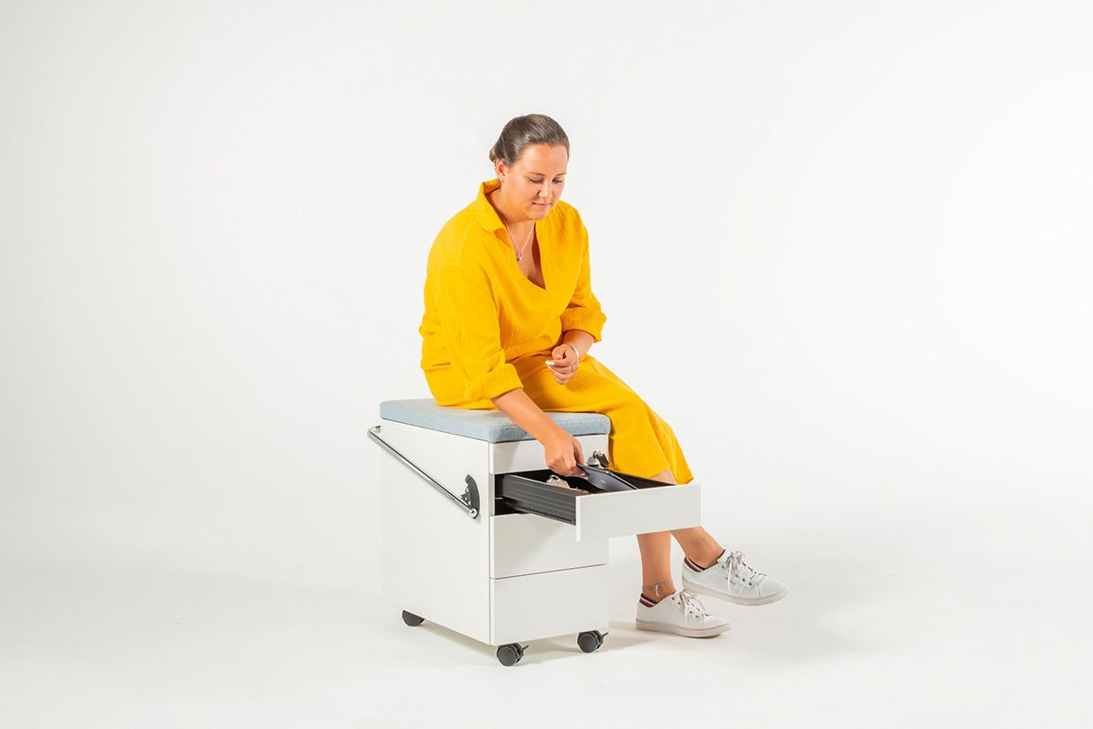Junge Frau in gelbem Kleid sitzt auf dem Rollcontainer OfficeBox von VS und greift in die Schublade.