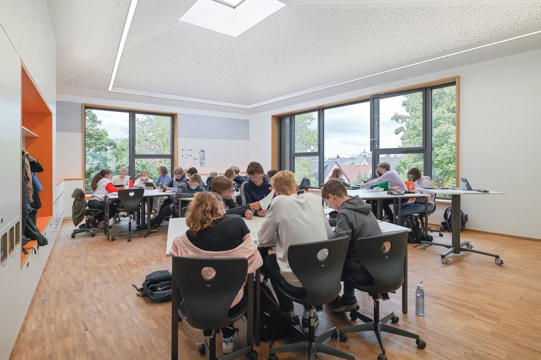 Classroom with pupils, black swivel chairs, white desks, wooden floor