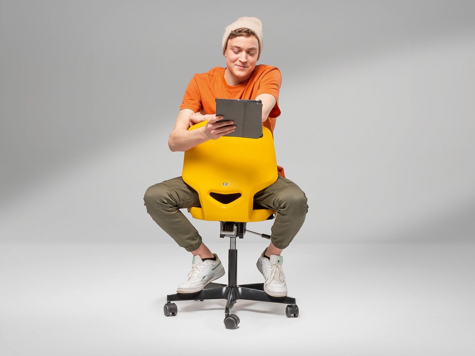 Ein junger Mann sitzt rittlings auf einem gelben JUMPER Air Drehstuhl von VS und schaut auf ein Tablet