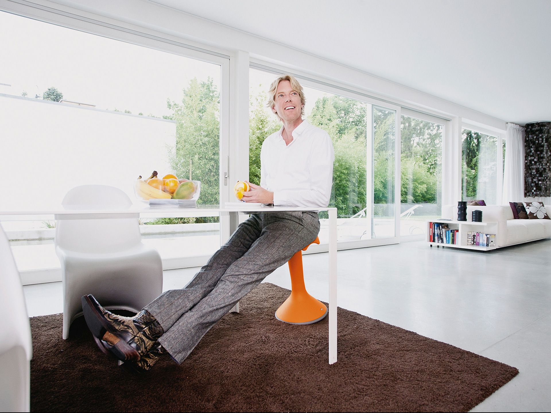 A middle-aged man sits at a table on the tilting orange stool Hokki by VS in a brightly decorated room