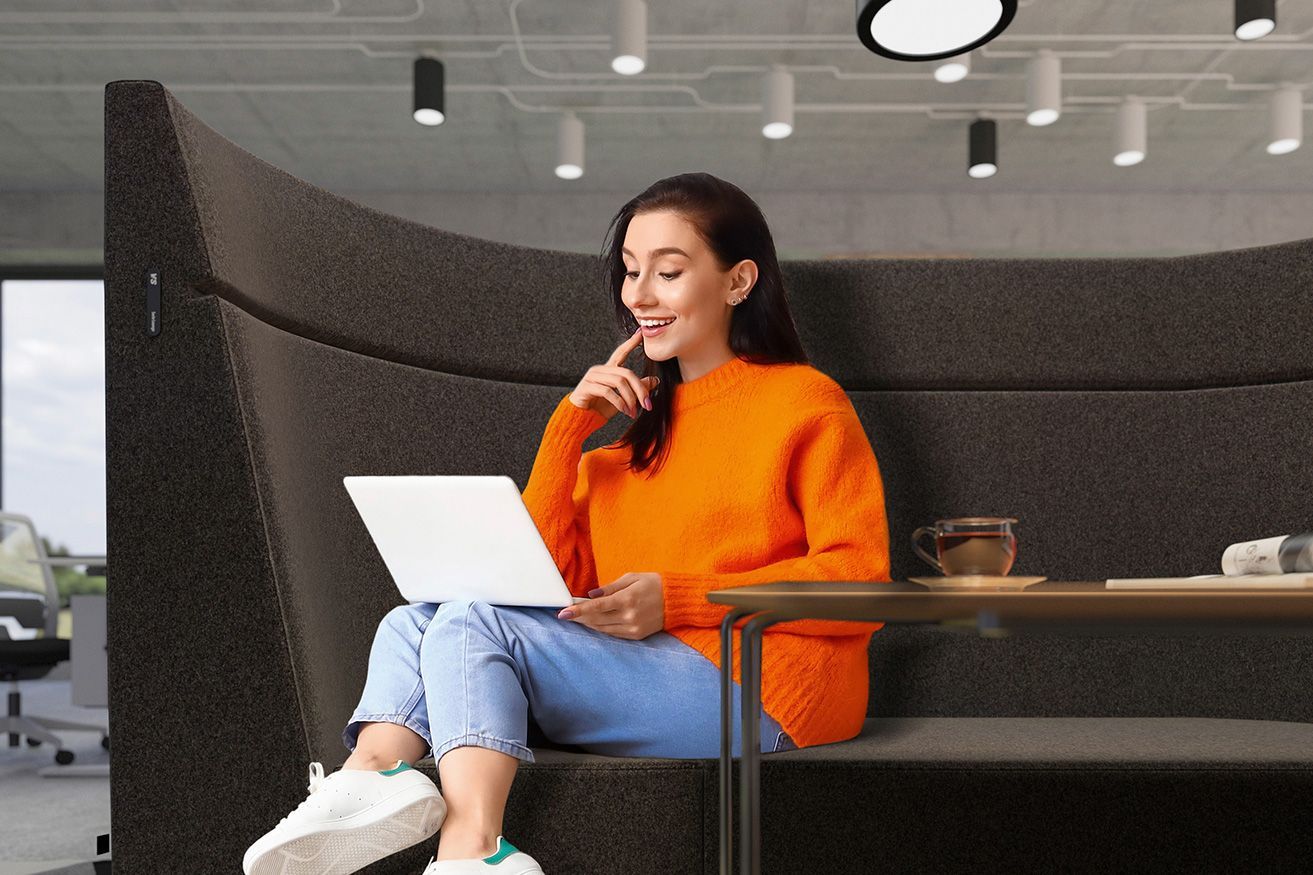 A woman works on her laptop in the semi-circular armchair with high backrest HiBack from the Lounge series by VS