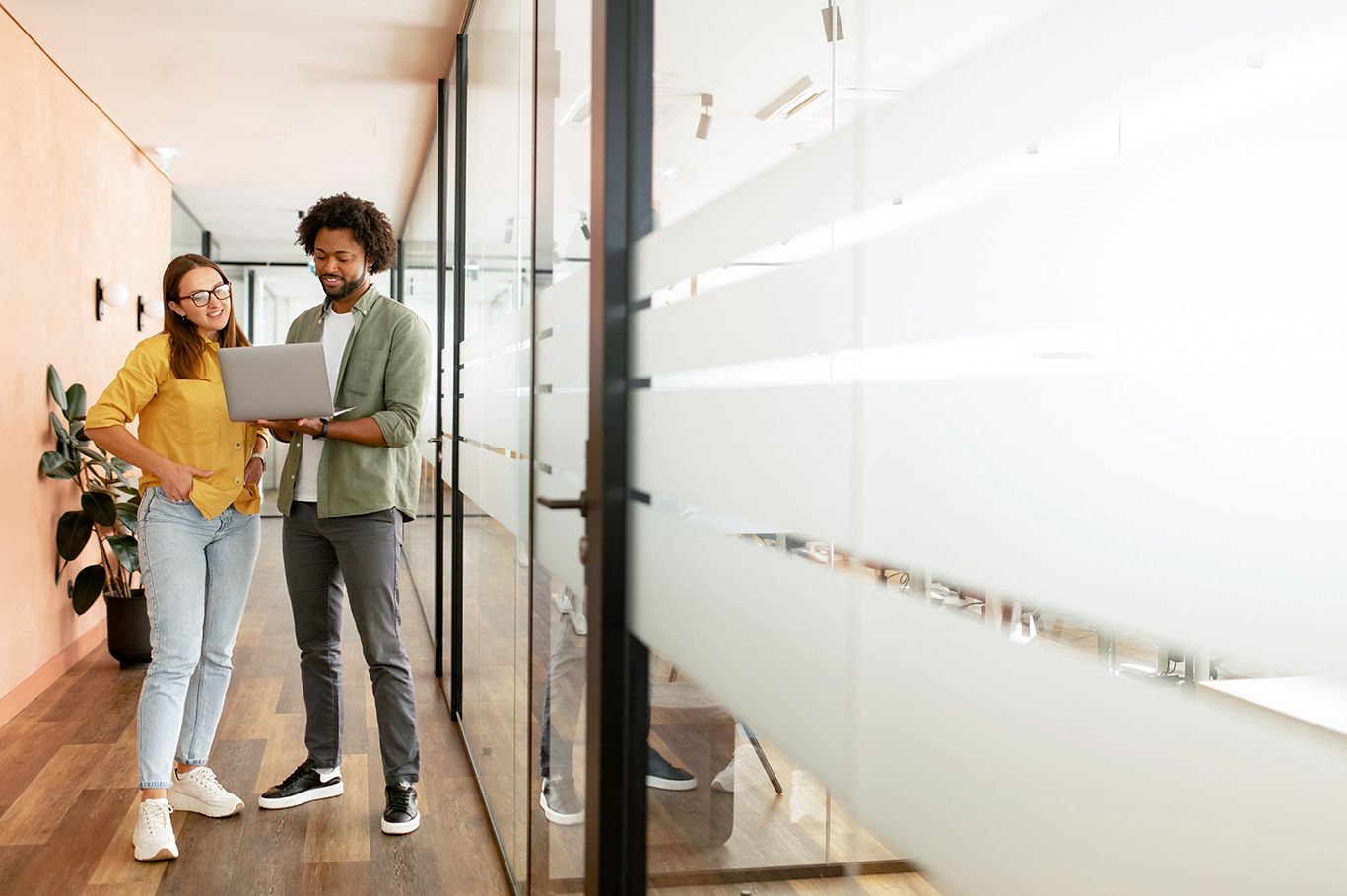 Two people are standing in the office looking at a laptop.