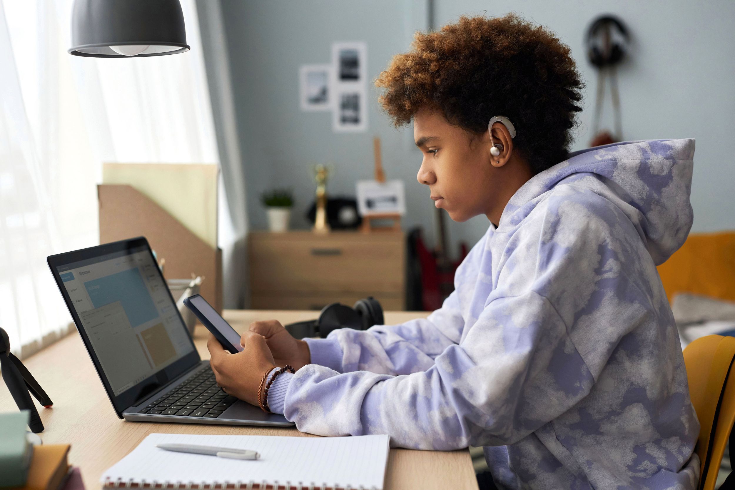 Junge am Schreibtisch mit Laptop und Smartphone